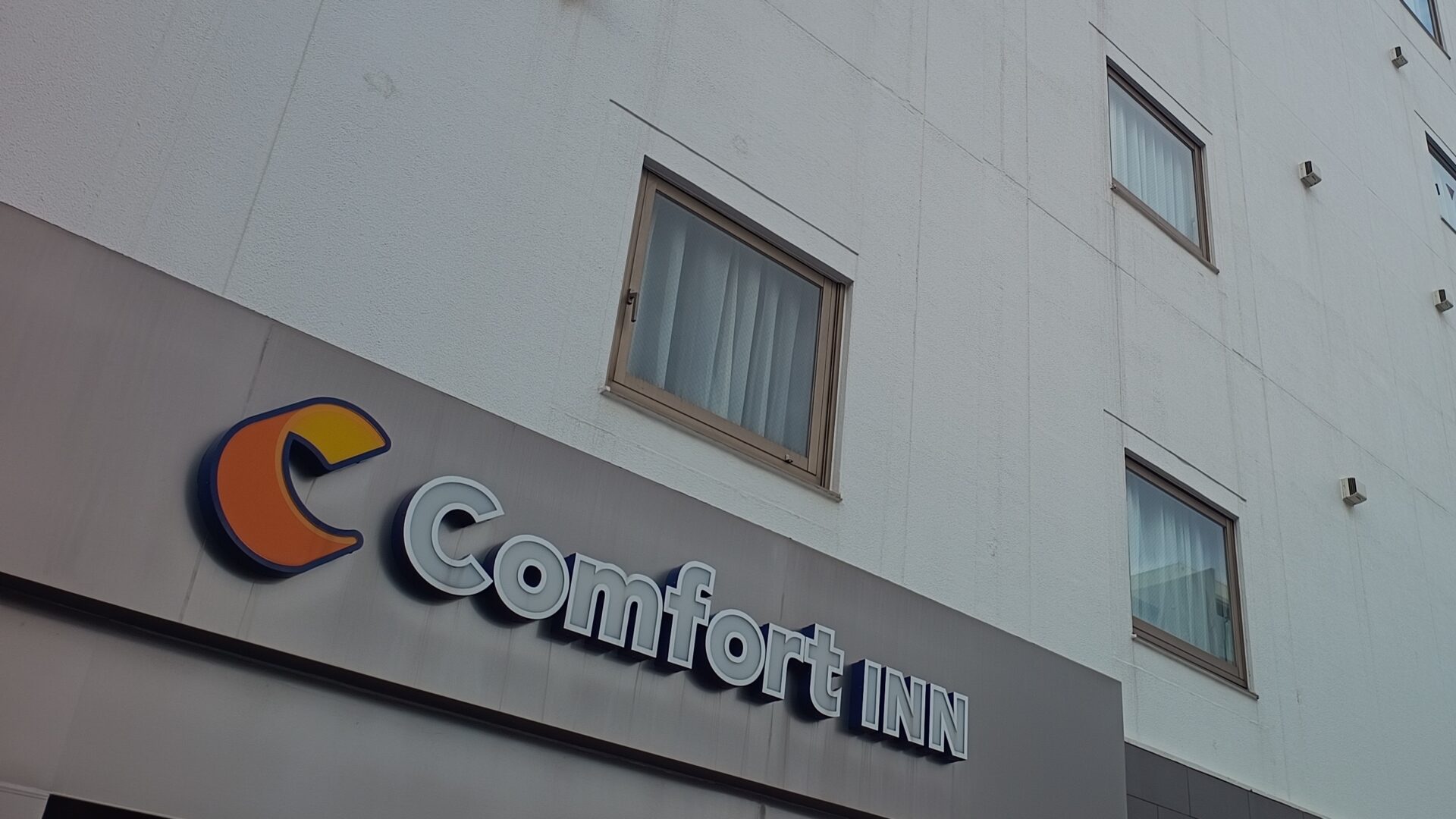 コンフォートイン那覇泊港の外観。Comfort INNの看板と客室の窓が見える