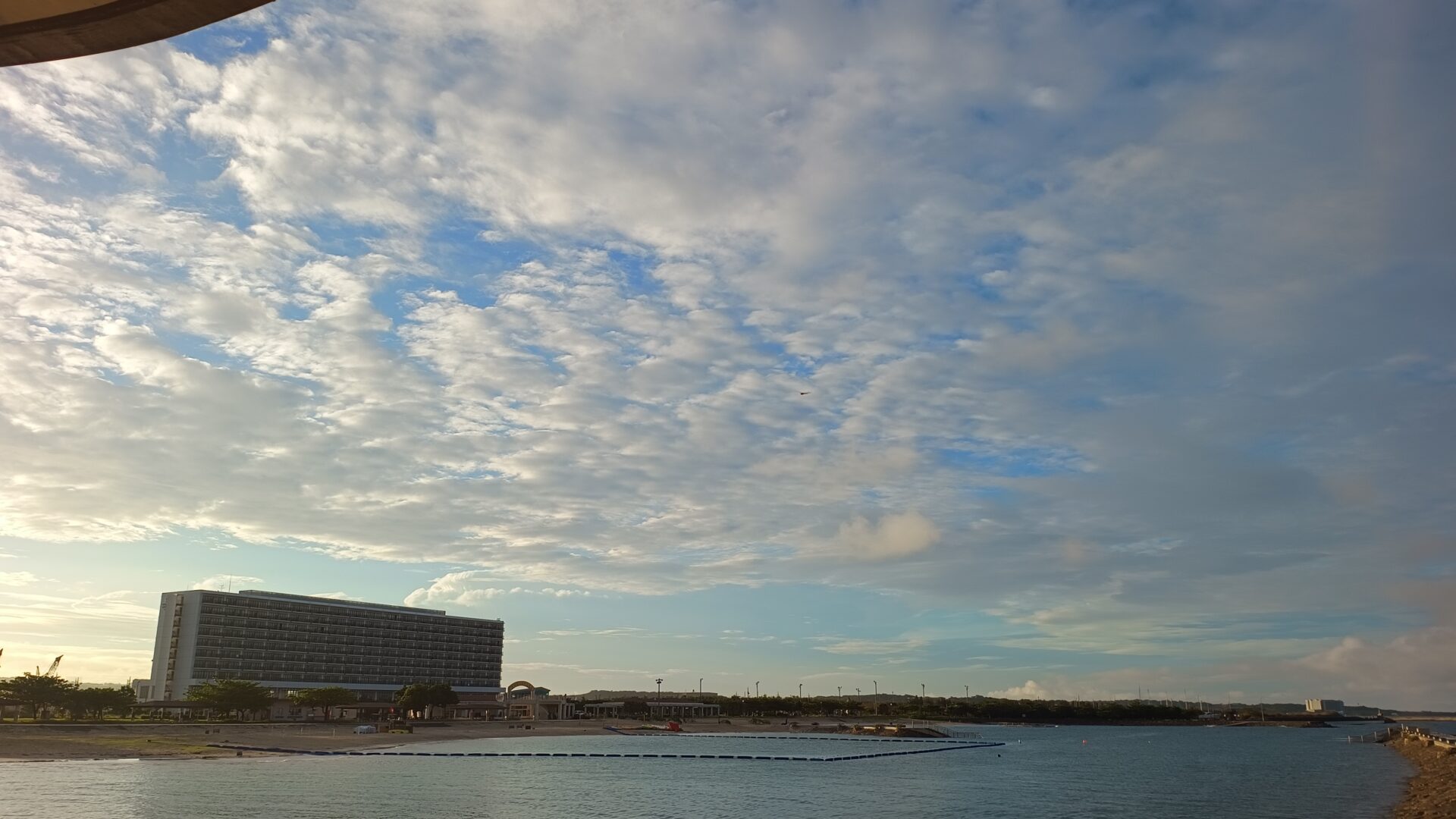 早朝の海から見た沖縄のリゾートホテルの外観。手前に砂浜と穏やかな海が広がっている